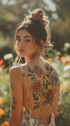 a woman with tattoos on her back standing in front of flowers