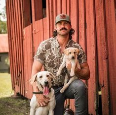 a man holding two dogs in front of a red barn with his tongue hanging out