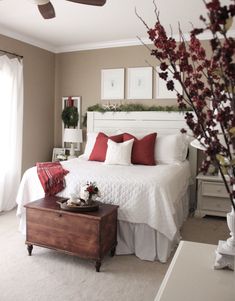 a white bed sitting next to a window with red pillows and blankets on top of it