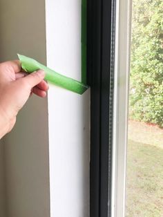 a person is holding a green piece of paper in front of a window sill