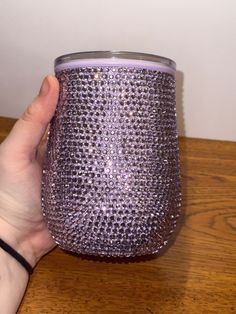 a hand holding a purple glass on top of a wooden table