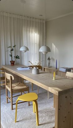 a wooden table with two chairs and a yellow stool in front of it on a white carpeted floor