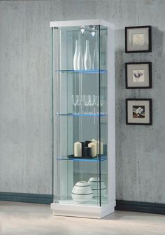 a glass display case with bottles and glasses on the bottom shelf in front of a gray wall