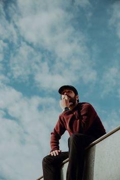 a man sitting on top of a cement wall talking on a cell phone with his hand in his mouth