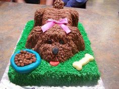 a dog cake with chocolate frosting and green grass on the top, has a bowl of dog food in front of it