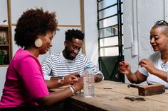 three people sitting at a wooden table playing with something in front of them and smiling