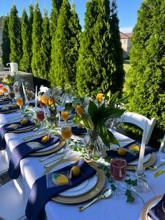 an outdoor table set with blue and white plates, silverware, flowers and napkins