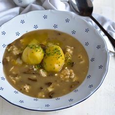 a white bowl filled with soup and potatoes on top of a table next to a spoon