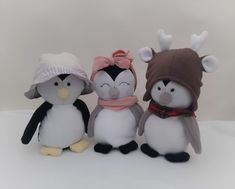 three stuffed penguins with hats and scarves are standing next to each other on a white surface