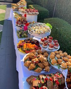 a long table filled with lots of different types of sandwiches and pastries on plates