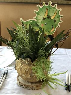 a green plant in a pot on top of a white table cloth with writing utensils next to it