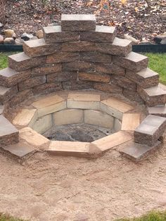 an outdoor fire pit made out of bricks in the middle of some grass and dirt