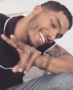 a man with tattoos on his arm making the peace sign while sitting in front of a white wall