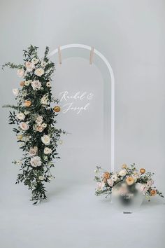 an arch decorated with flowers and greenery stands next to a vase filled with roses