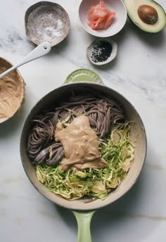 an avocado and pasta dish with sauce in a skillet on a marble countertop