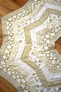 a quilted table runner with gold and white designs on it, sitting on a wooden floor