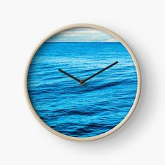 a clock that is on the side of a wall in front of some blue water