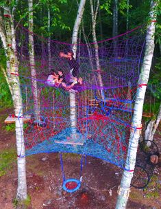 two people are playing on a rope course in the woods while another person watches from above