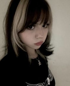 a woman with long hair wearing a black t - shirt and silver necklace, standing in front of a white wall