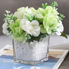 a vase filled with white and green flowers on top of a table next to a book