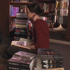 a woman sitting on the floor reading a book in front of a bookshelf