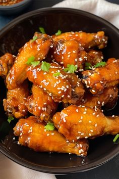 a black bowl filled with chicken wings covered in sesame seeds and garnished with parsley