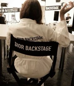 a woman sitting in a chair with her back turned to the camera and she is wearing a white jacket that says dior backstage