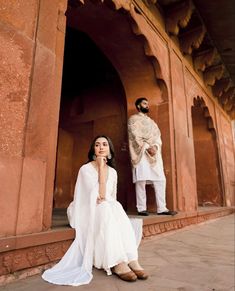 a woman sitting on the ground next to a man in a white suit and turban