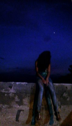 a woman sitting on top of a cement wall next to a fire hydrant at night