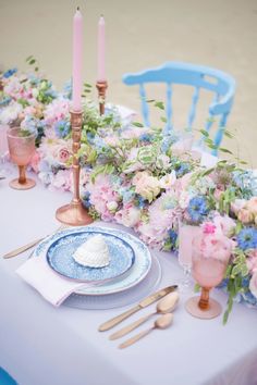 the table is set with pink and blue flowers, gold candles, and silverware