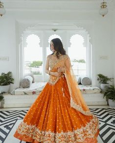 a woman in an orange lehenga standing on a black and white patterned floor