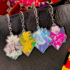 three keychains with cartoon characters on them hanging from a black leather bag next to flowers