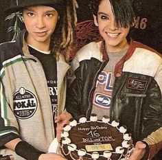 two young people standing next to each other holding a cake