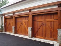 three wooden garage doors in front of a white house with stone pillars and brick columns