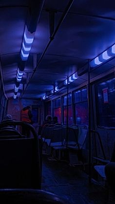 the inside of a bus at night with blue lights and people sitting on seats in it