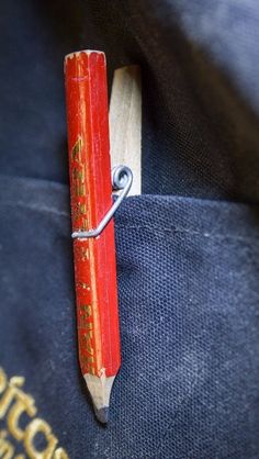 an old red pencil is tied to a blue book bag with gold lettering on it