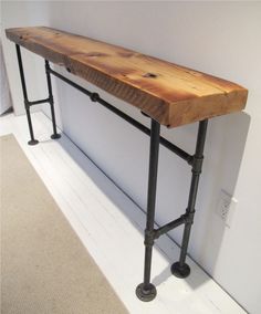 a long wooden table sitting on top of a metal pipe frame next to a wall