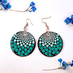 a pair of blue and black earrings with circles on them, sitting next to flowers