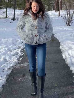 a woman walking down a snow covered path wearing boots and a jacket with buttons on it