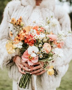 a woman holding a bouquet of flowers in her hands and wearing a white fur coat