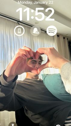 a person making a heart shape with their hands while standing in front of a window