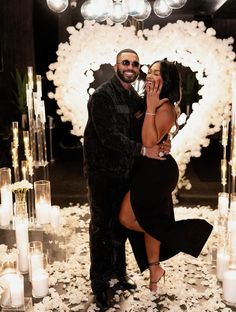 a man and woman standing next to each other in front of white flowers with candles