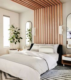 a white bed sitting in a bedroom next to two mirrors and a potted plant