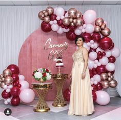 a woman standing in front of a cake on a table next to balloons and flowers