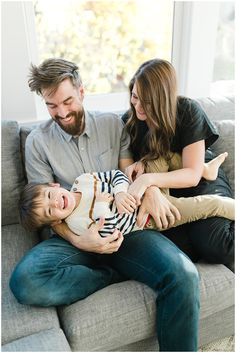 a man, woman and child are sitting on a couch smiling at each other as they hold their baby