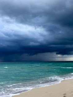 an ocean beach with waves crashing on the shore and dark clouds in the sky above