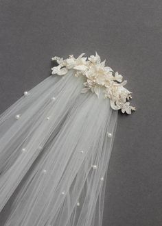 wedding veil with flowers and pearls on the side, laying flat against a gray background