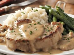 a white plate topped with meat and gravy next to green beans