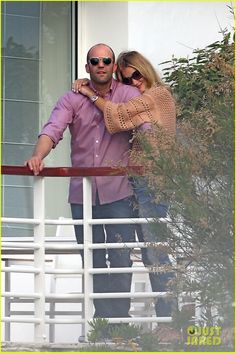 a man and woman standing on a balcony next to each other with their arms around each other