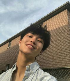 a young man standing in front of a brick building holding a cell phone up to his ear